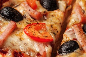 Letterbox panorama of sliced ham pizza with capsicum and olives on wooden board on table